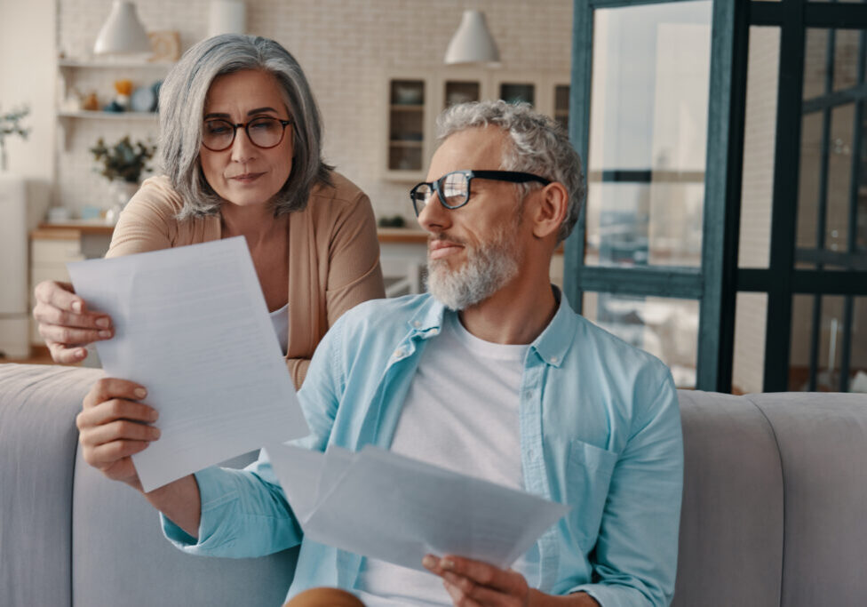 Busy senior couple in casual clothing doing paperwork while bonding together at home