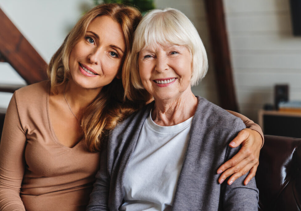 Close up portrait of elderly mother and middle aged daughter smiling together on the couch at home