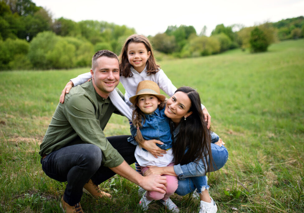 Front view of happy family with two small daughters sitting outdoors in spring nature, looking at camera.