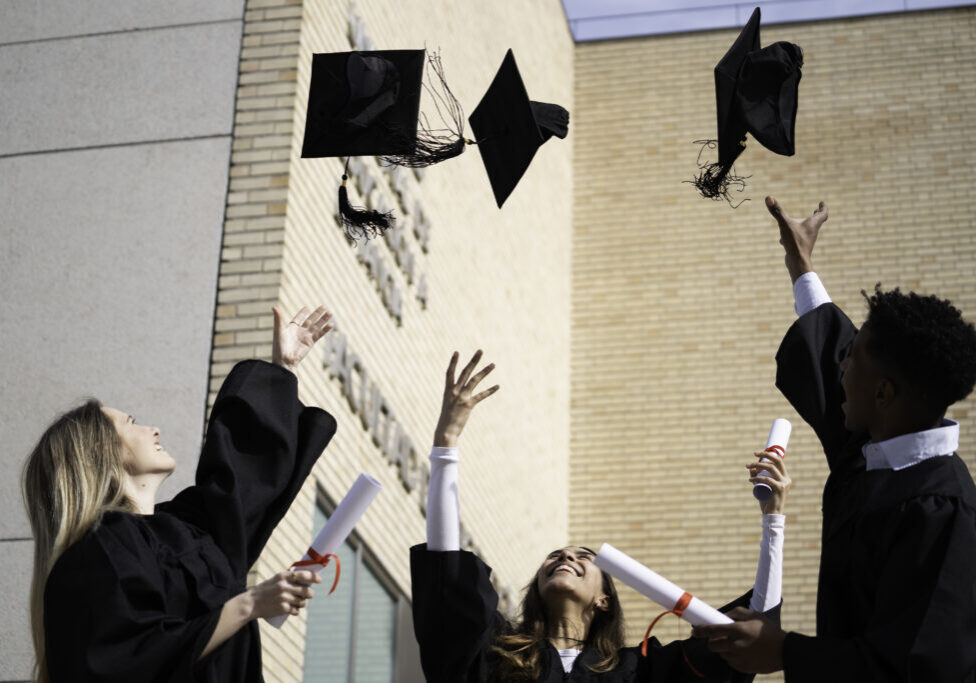 Group of cheerful multi-ethnic students in graduation gowns throwing their caps in the air after receiving their diplomas