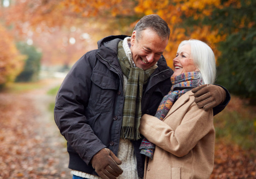 Loving Senior Couple Hugging As They Walk Along Autumn Woodland Path Through Trees Loving Senior Couple Hugging As They Walk Along Autumn Woodland Path Through Trees