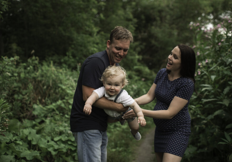 Pregnant couple swinging toddler son on pathway