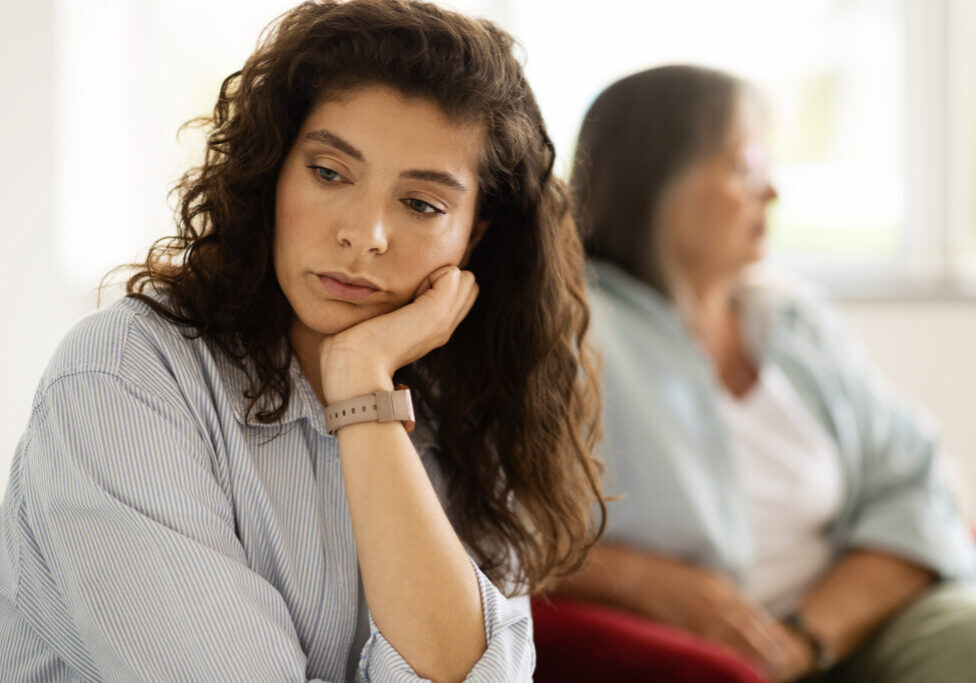 Sad adult caucasian woman ignoring unhappy angry older lady after quarrel in living room interior. Family problems, female generation, mother daughter relationship, stress and scandal