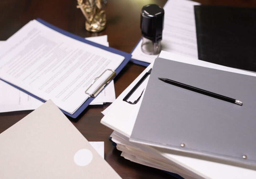 Part of table with stacks of juridical and business documents in folders and clipboards with pencil on top
